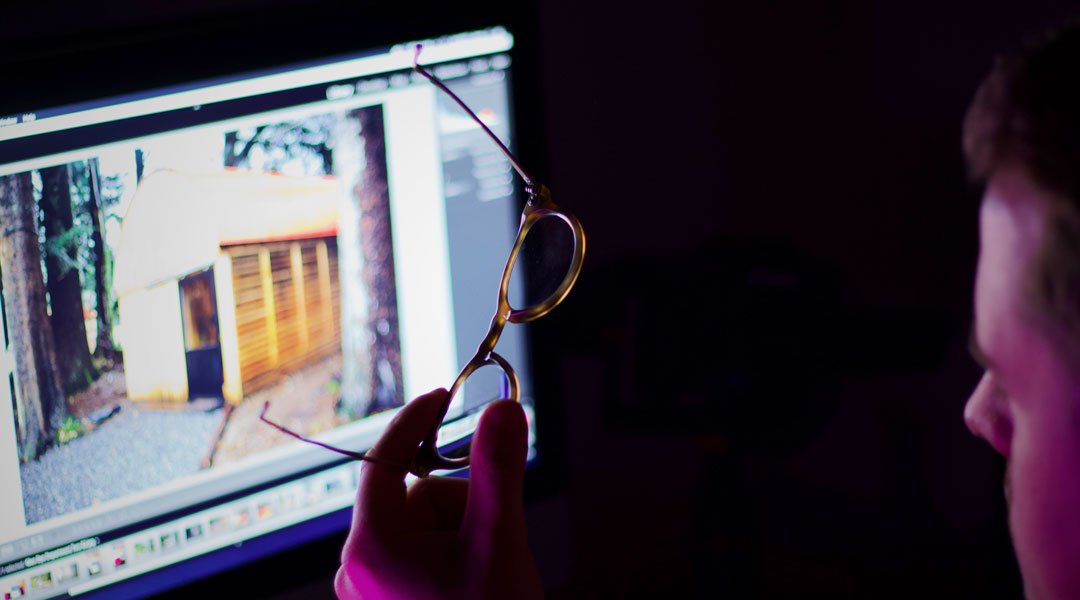 Man holding a pair of blue light glasses in front of a computer screen