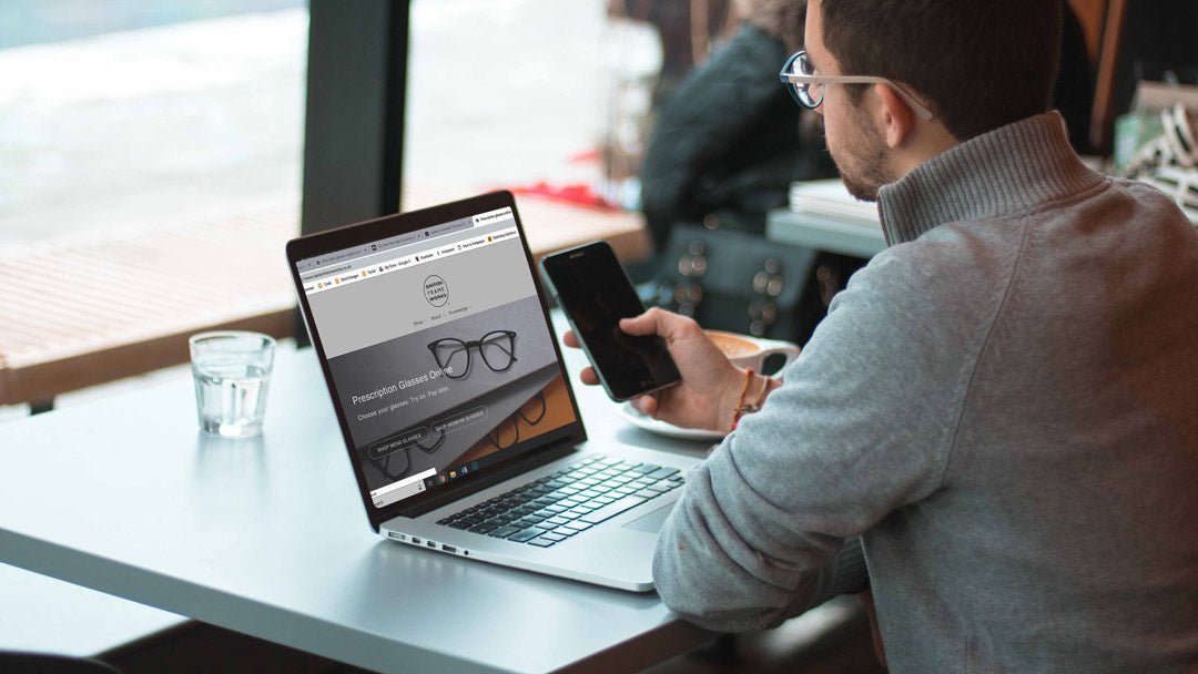 Man wearing glasses using both his laptop and phone screens