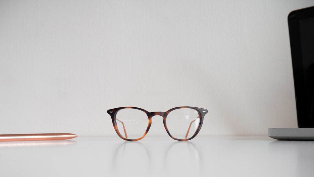 Tortoise acetate computer glasses sitting on white desk beside laptop computer