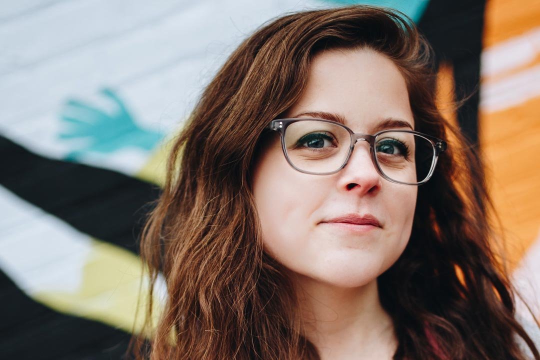 Brown haired lady wearing square grey eyeglasses looking directly at viewer