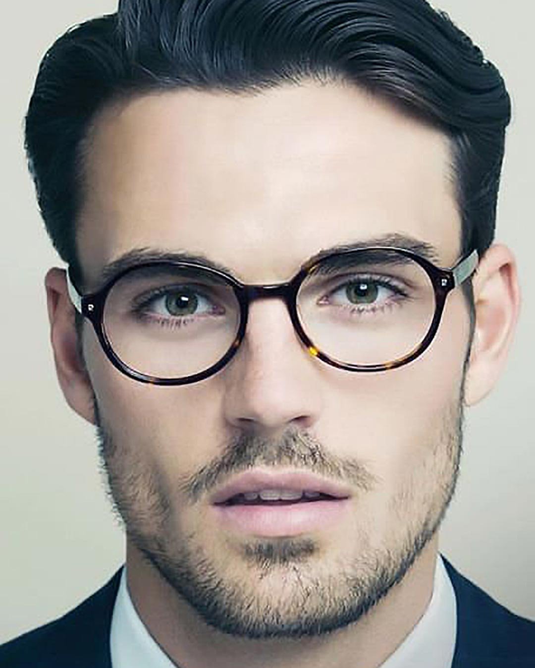 Man with dark hair and beard wearing oval tortoiseshell spectacles